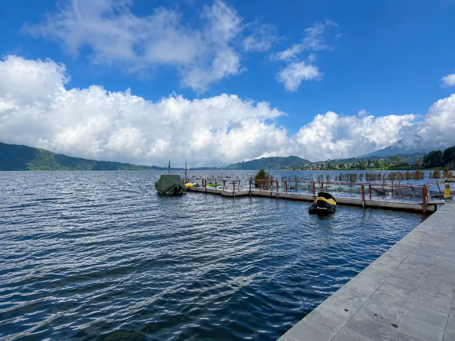 Wide view across Lake Buyan from the jetty, with forested hills and cloud above the water.