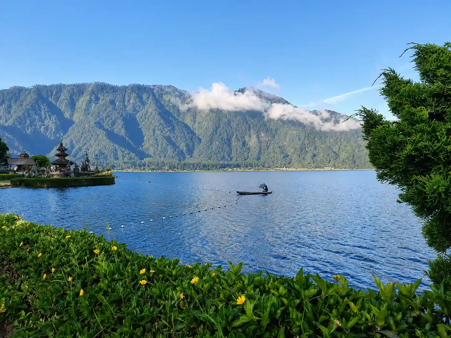 Lake Beratan with a lakeside Balinese temple, a fisherman in a canoe and forested mountains behind.